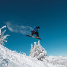 Java Snow Note Bender snowboard under the feet of snowboarder in the air with bluebird conditions.